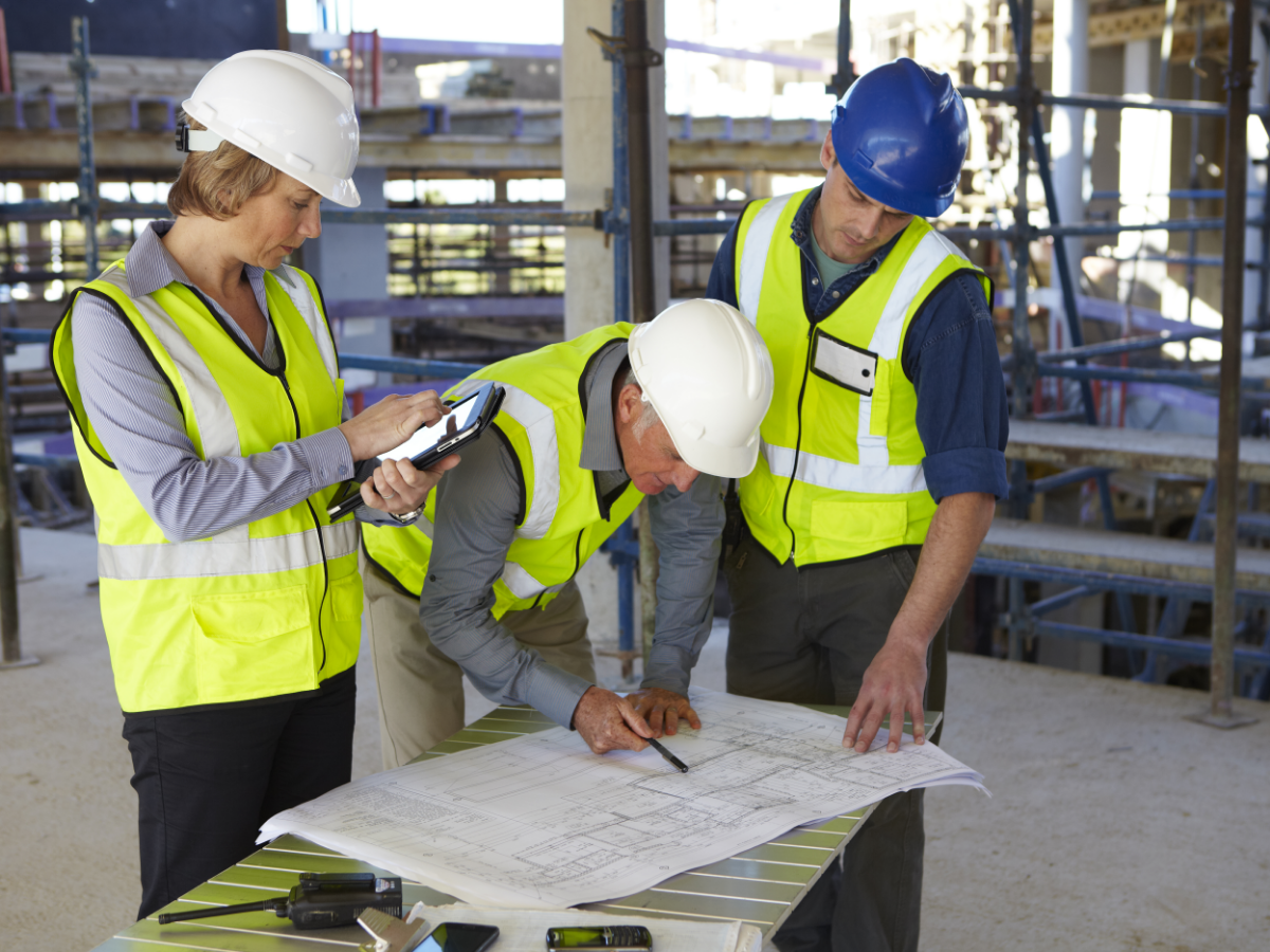 people in safety gear looking at blue prints on construction site