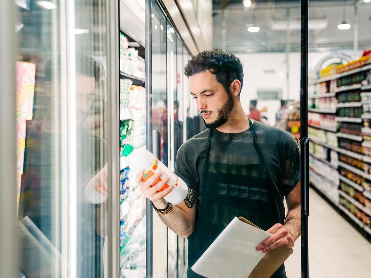 male grocery store employee reading nutrition label on a drink in fridge section