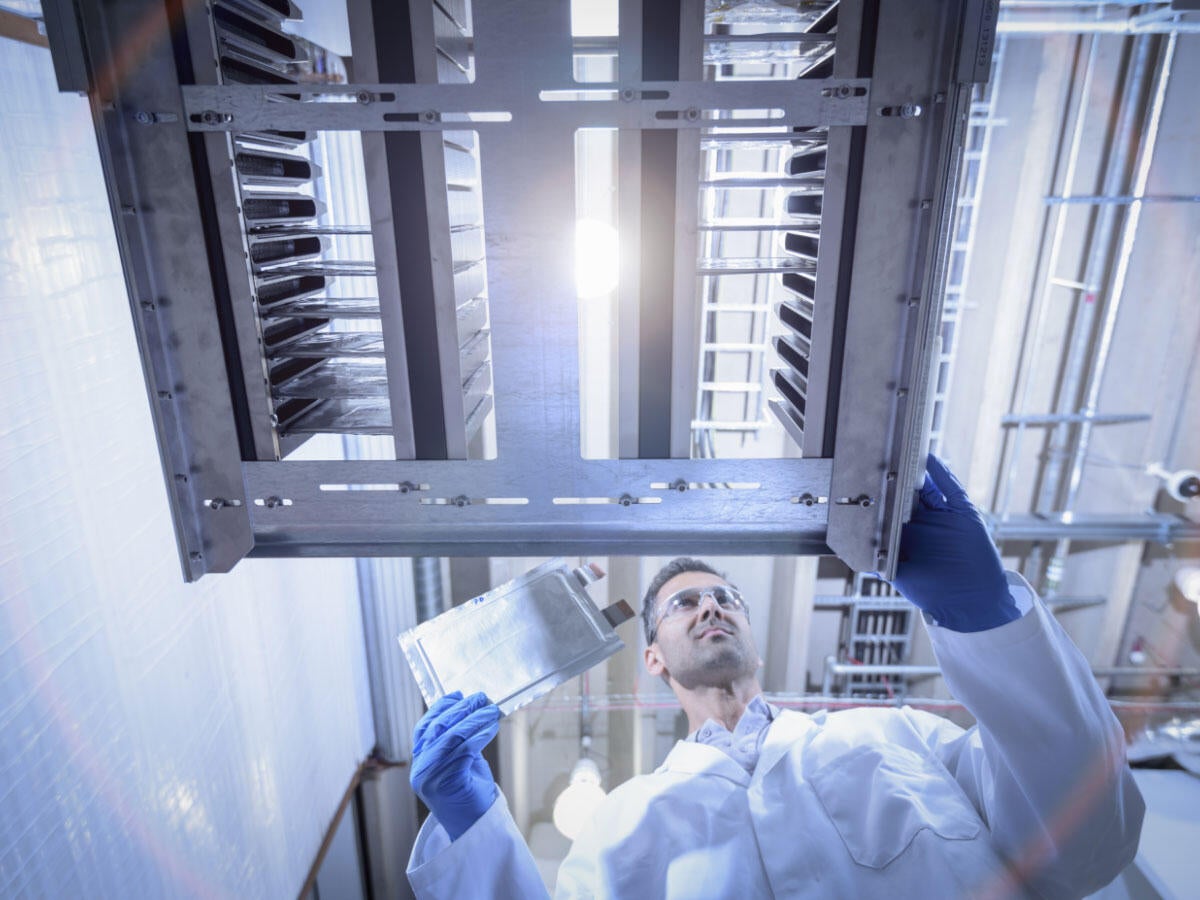 Scientist with lithium ion pouch cell manufacture machine in battery research facility, low angle view
