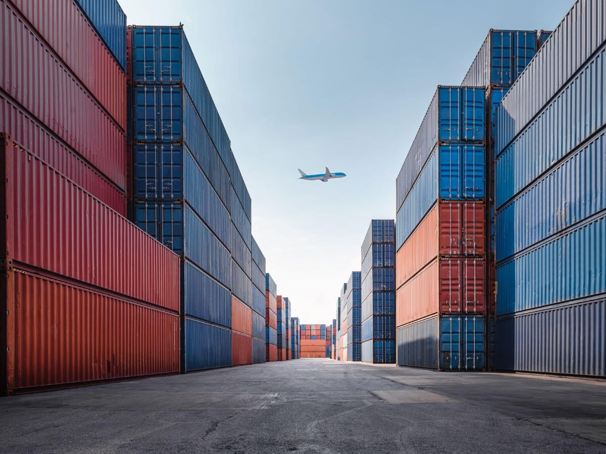 A plane flying in the background of rows of storage containers