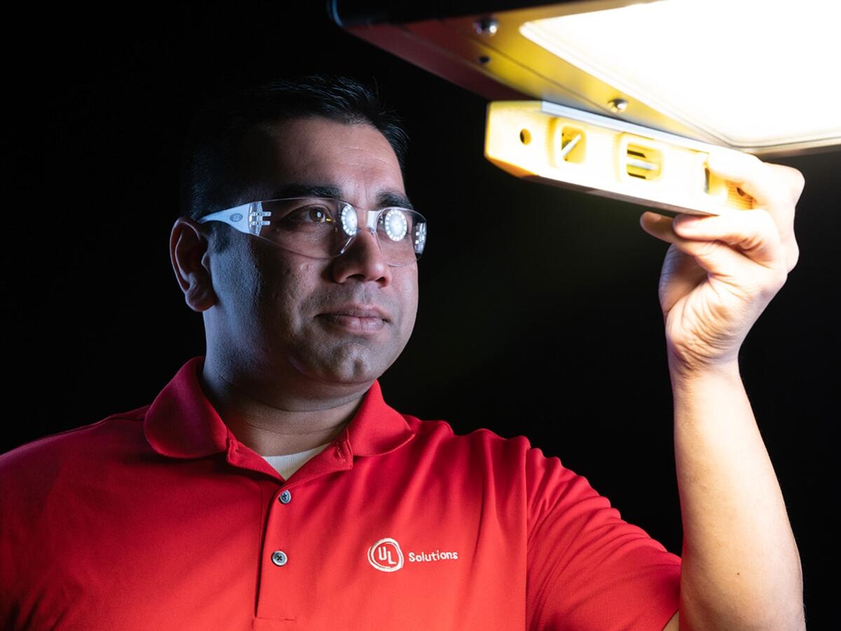 Person in a red UL Solutions shirt holding a yellow level under a bright overhead light.