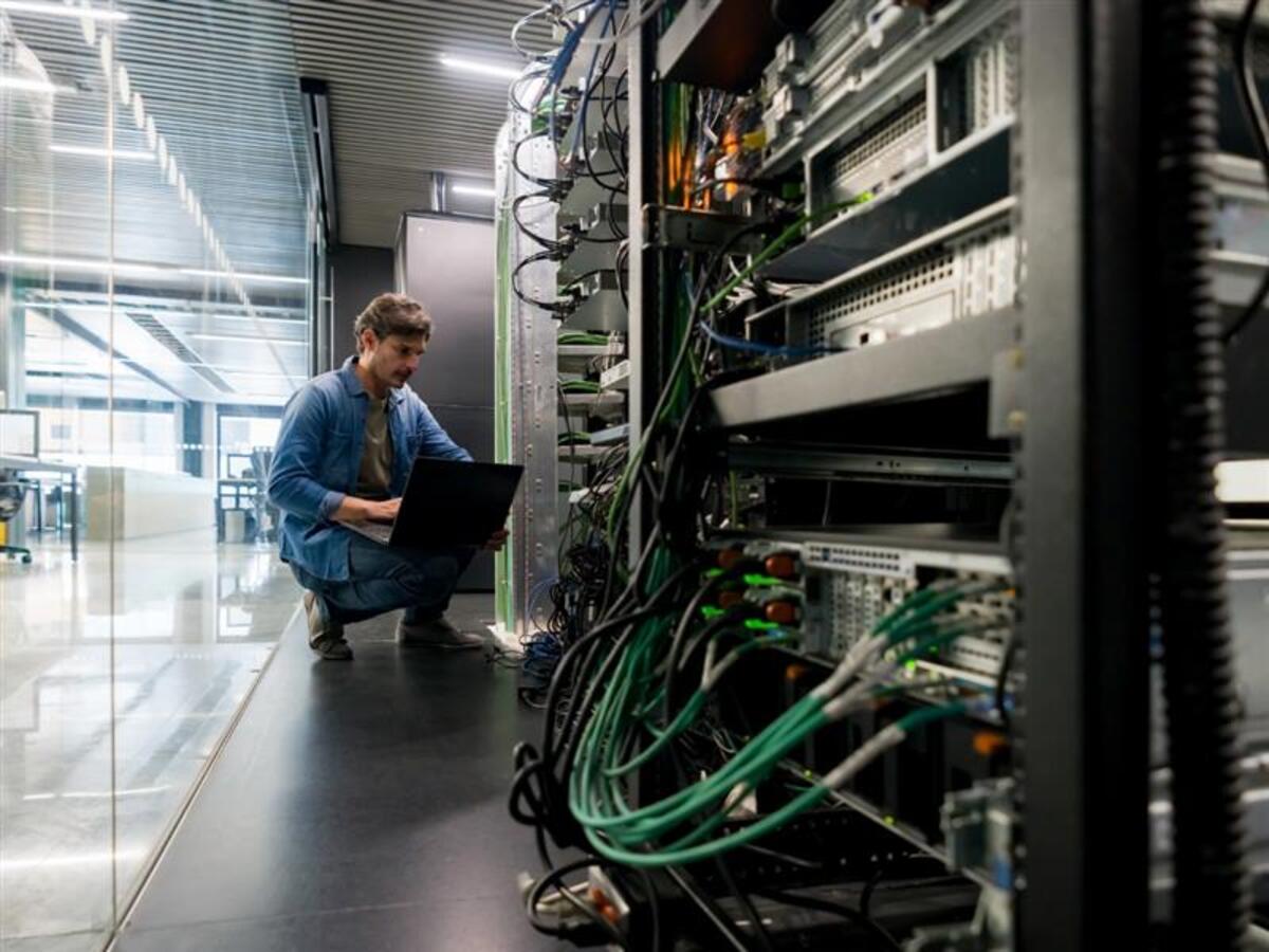 Technician working on a laptop beside server racks in a data center.