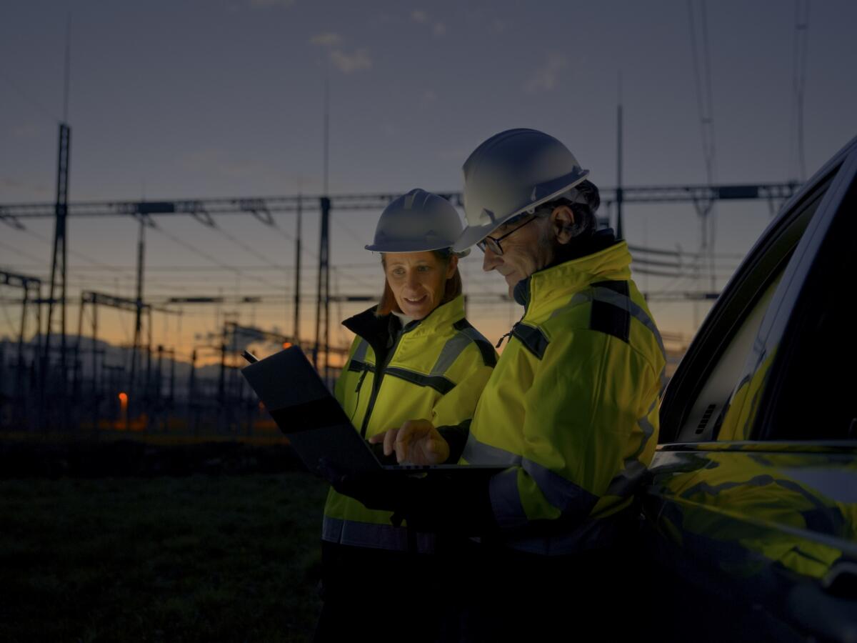 Two engineers looking at reports while standing next to a power grid at dawn