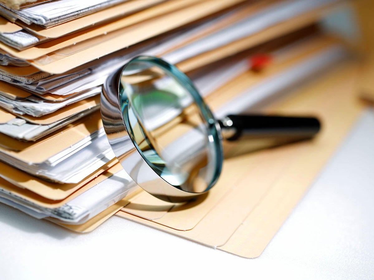 Magnifying glass resting on a stack of manila folders and documents
