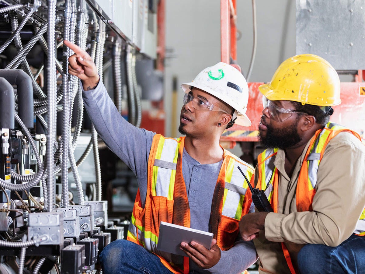 Two workers in safety vests and helmets inspecting electrical equipment