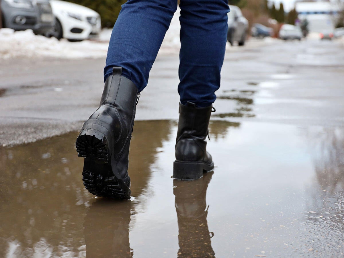 A person wearing boots and walking over a puddle