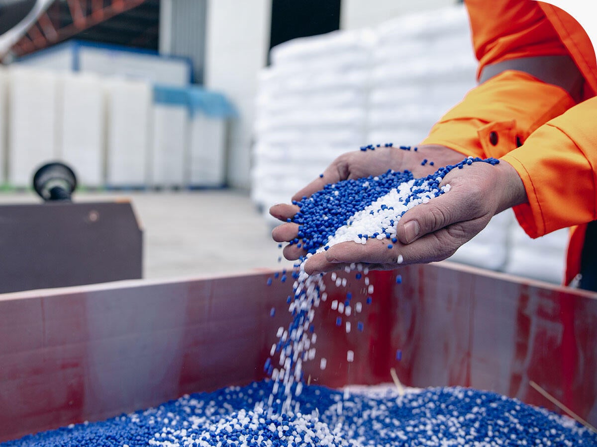Person in warehouse picking up handfuls of blue and white chemical pellets