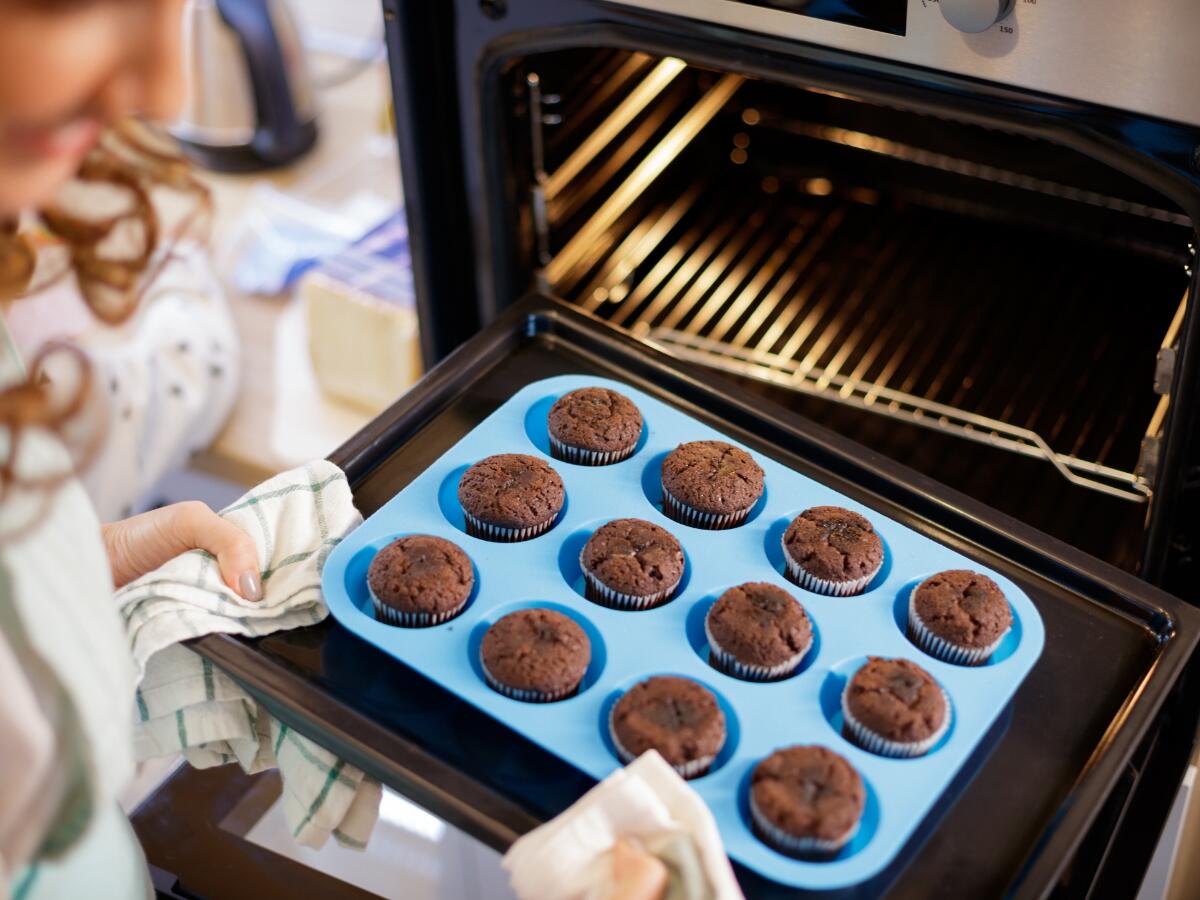 A person removing muffins baked in a silicone cupcake pan out of the over
