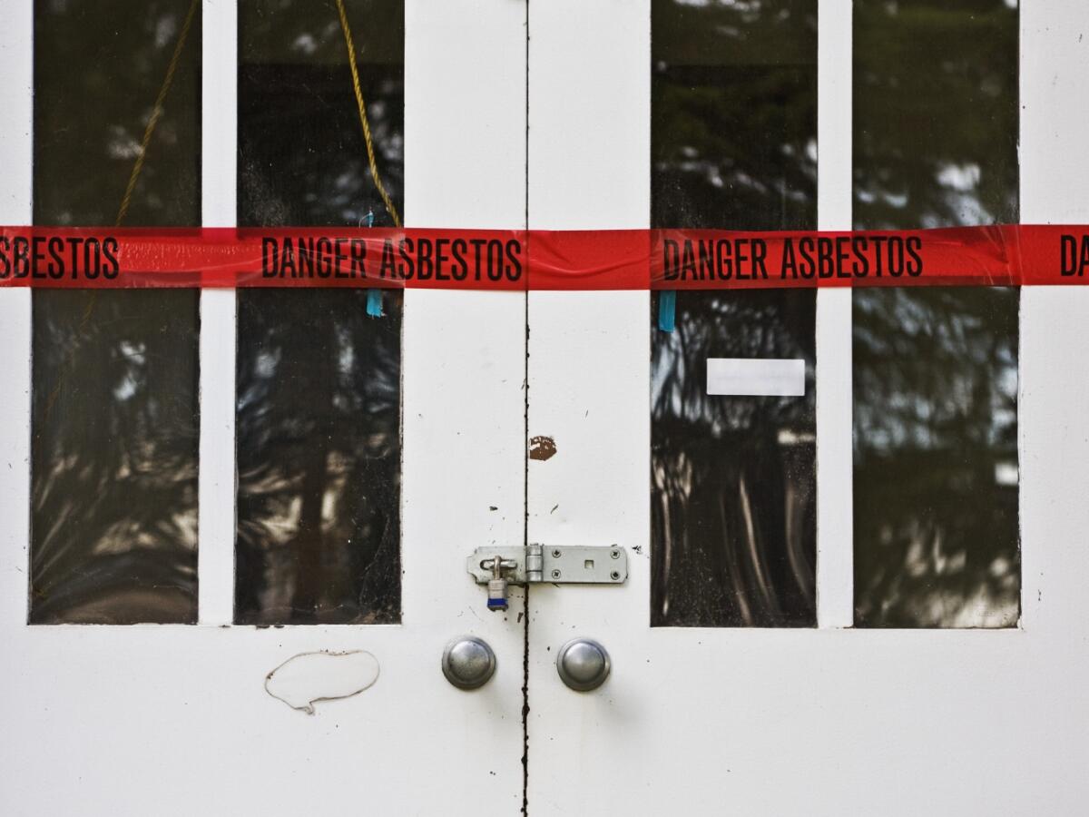 Closed and locked double doors with red tape warning of asbestos 