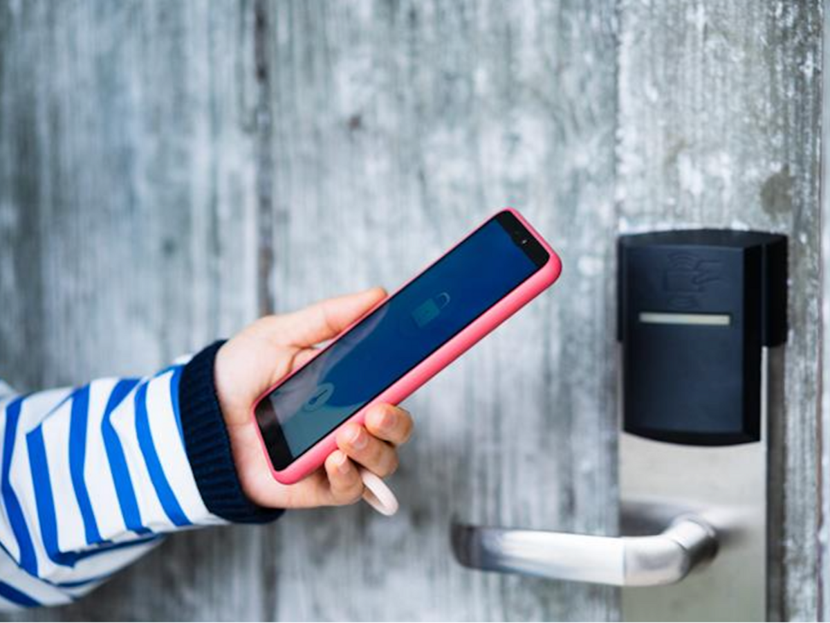 Woman in blue striped shirt holding a smart phone next to a digital lock