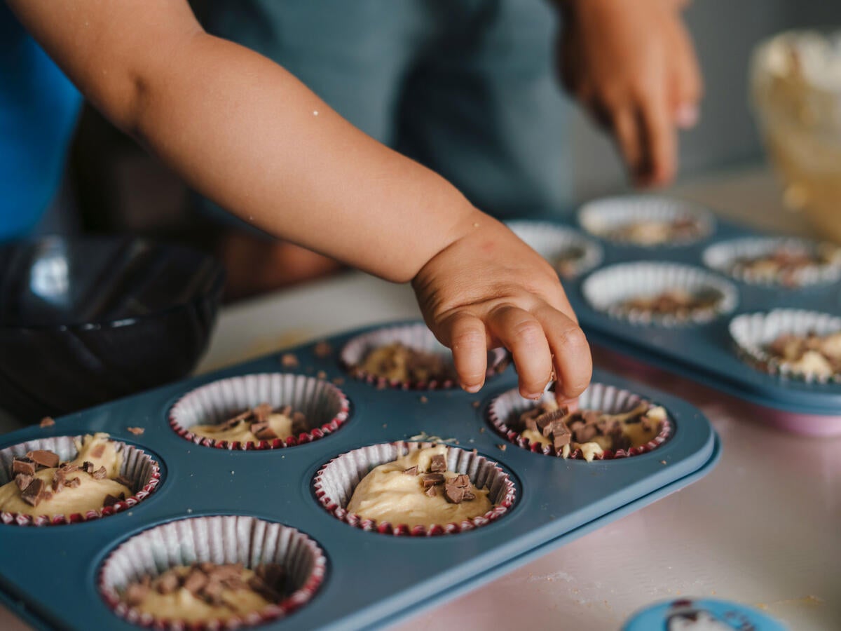 Small child reaching for an uncooked cupcake in a baking tray