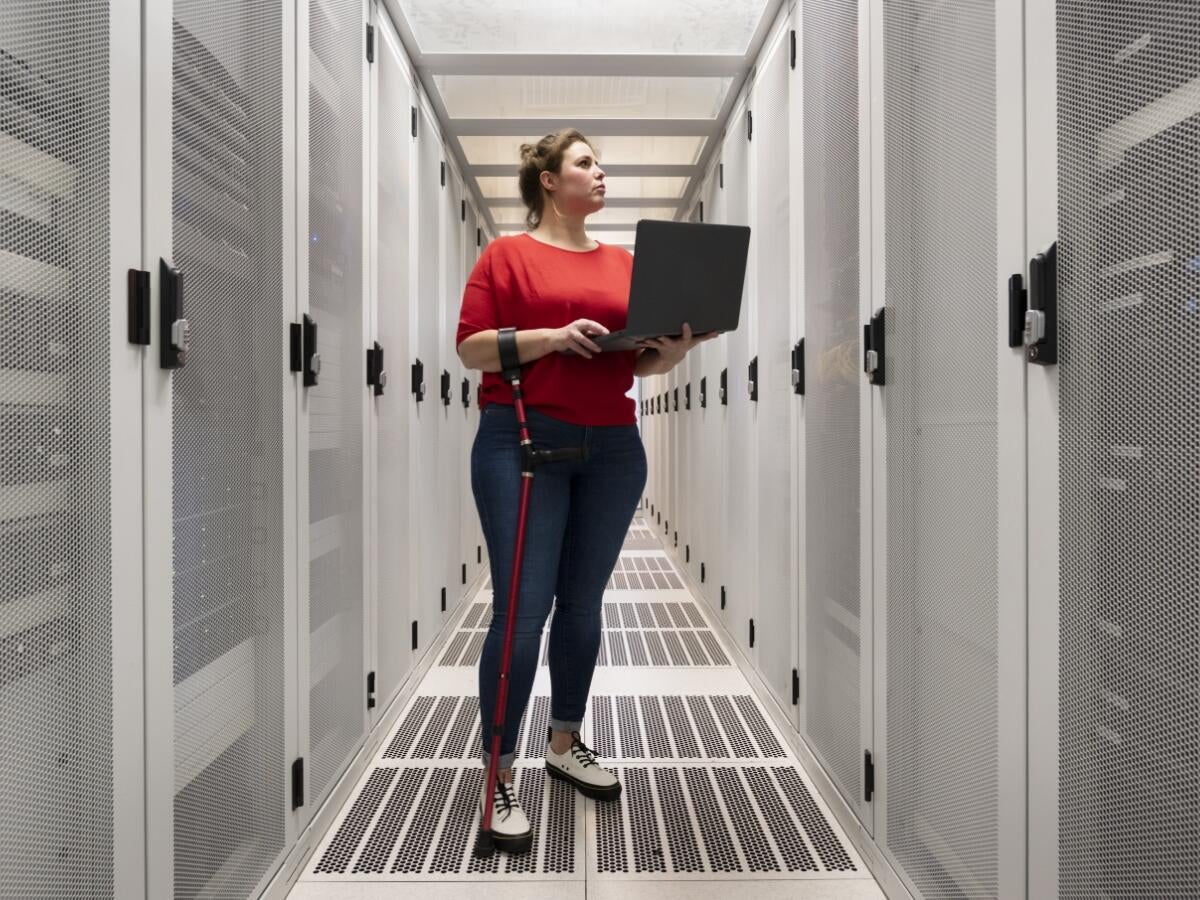 Technician holding a laptop while inspecting a server rack in a data center