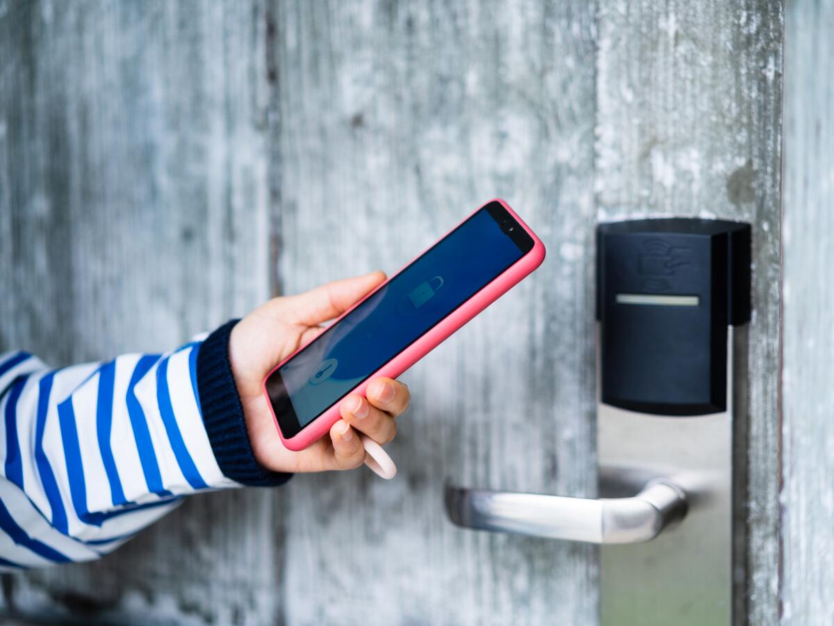 Person holding smartphone next to digital door lock.