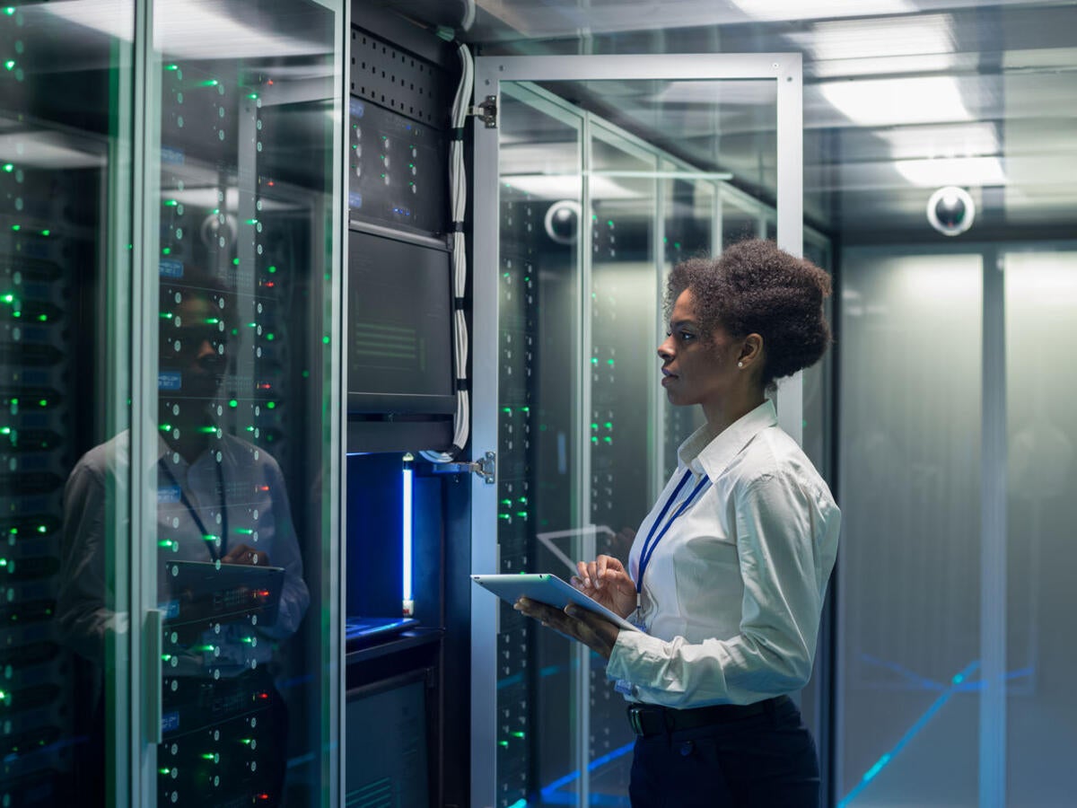 Technician working on a tablet in a data center full of rack servers running diagnostics and maintenance on the system.