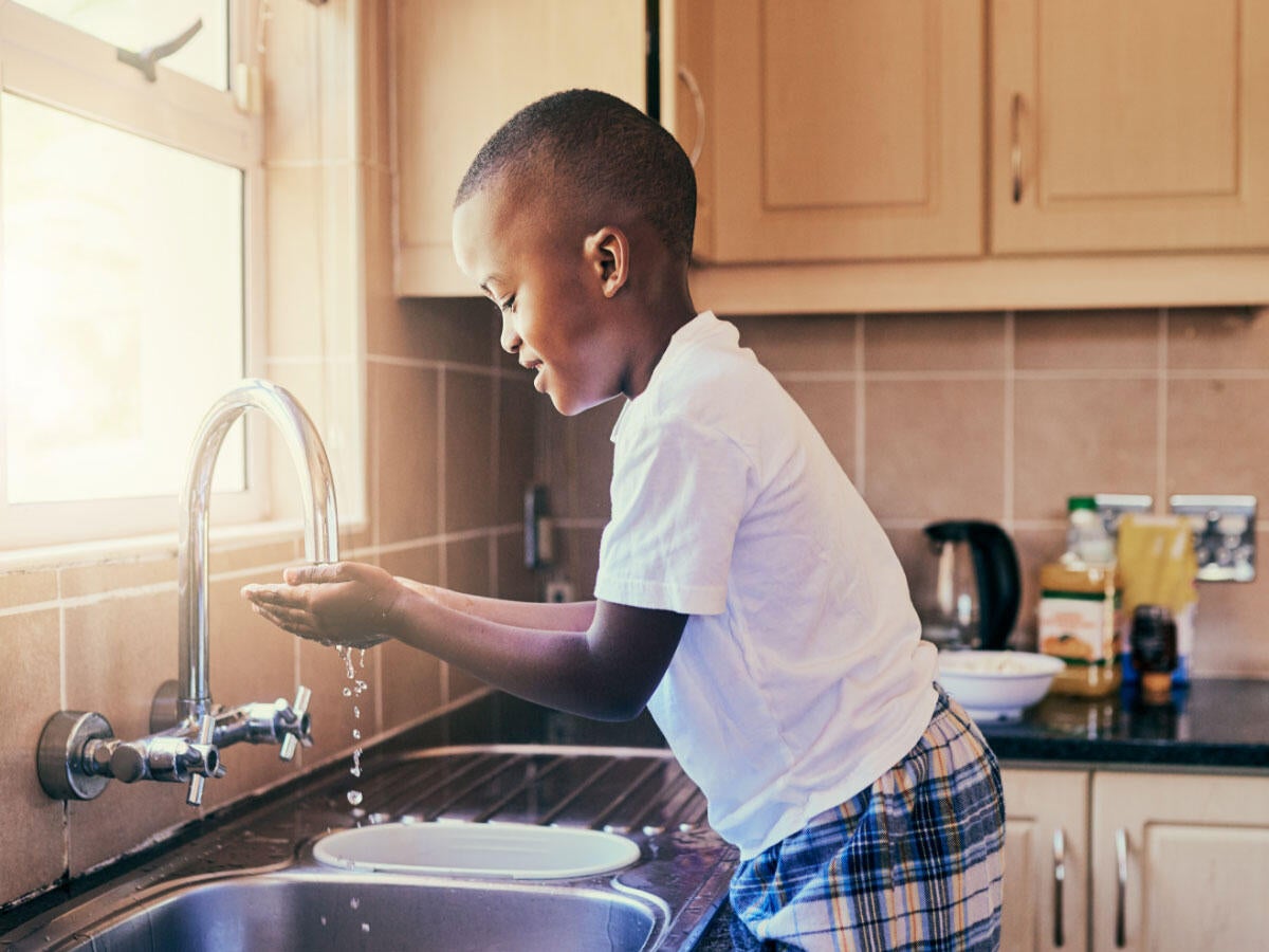 A young child washing hands at a kitchen sink