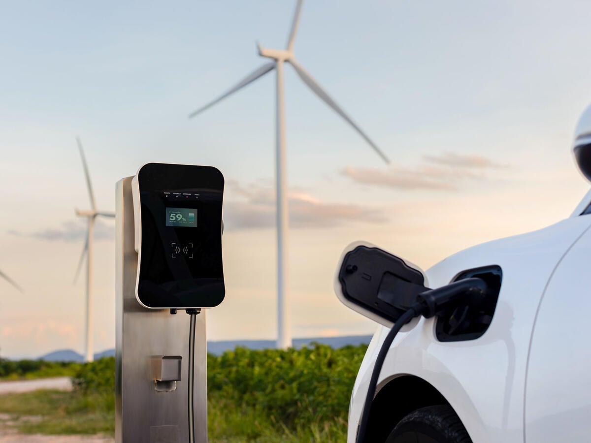 An EV charging at a charging station with wind turbines in the background