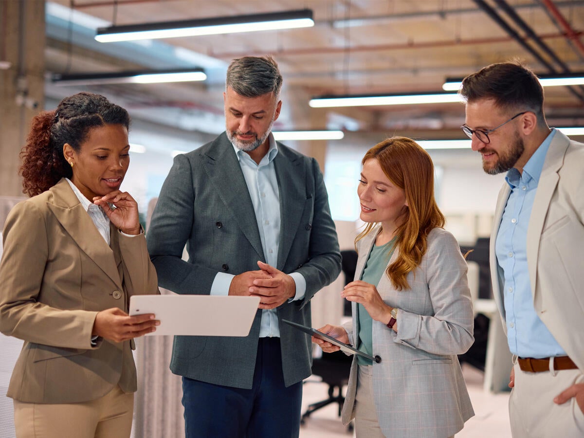 people in office environment all gathered around a woman with a tablet