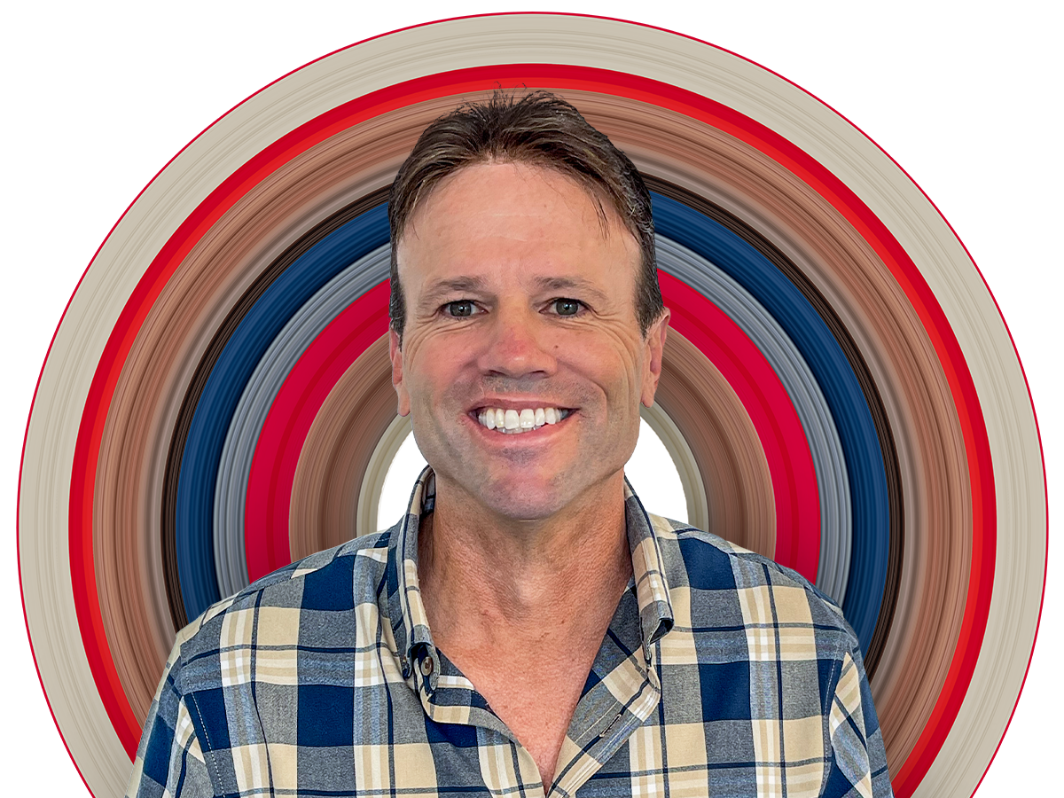 Sales manager Tony smiles at the camera wearing a blue and cream plaid shirt with the top button undone. He has neat brown hair cut short.