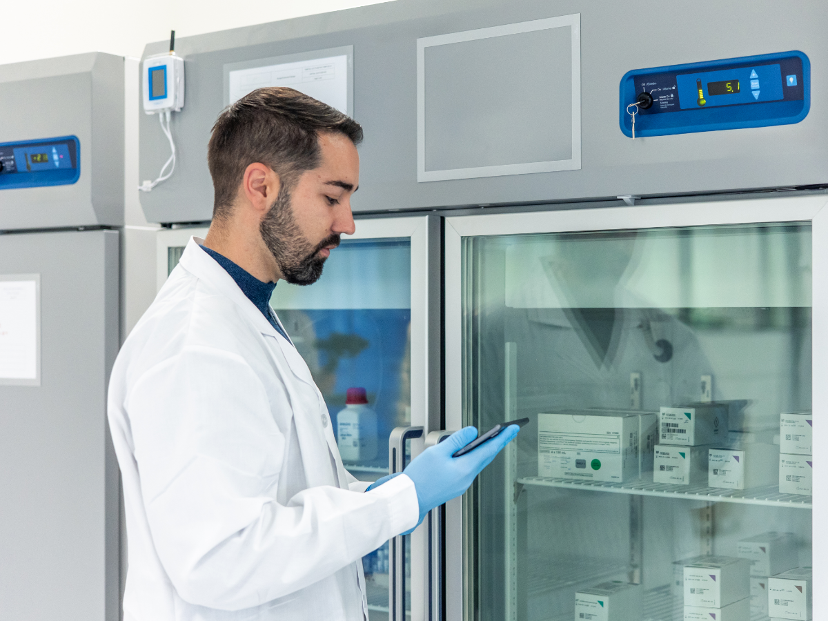 Scientist using a digital tablet near a laboratory refrigerator storing medical samples