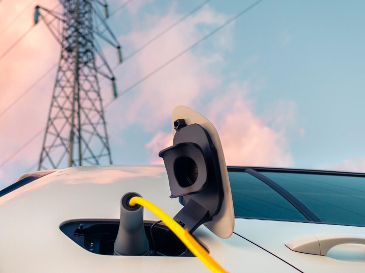 EV connected to a charging station in the foreground, with transmission towers or utility power lines clearly visible in the background.