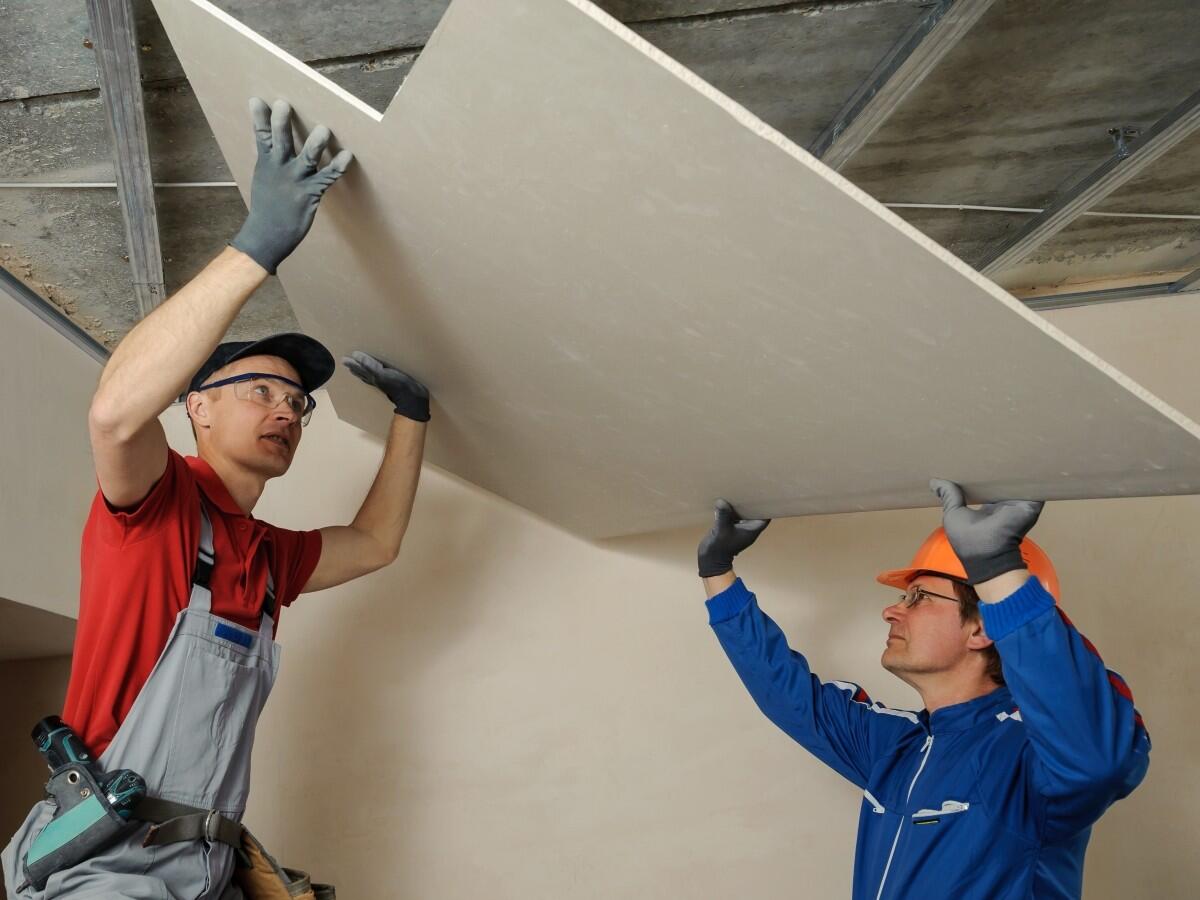 Two mean in hardhats install gypsum board to a ceiling