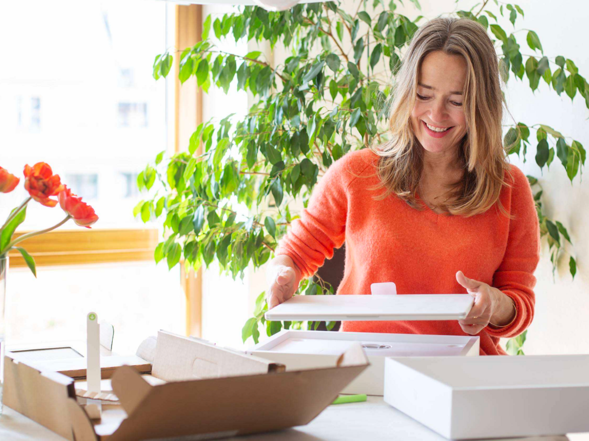 Woman in orange sweater opening a boxed package on a table