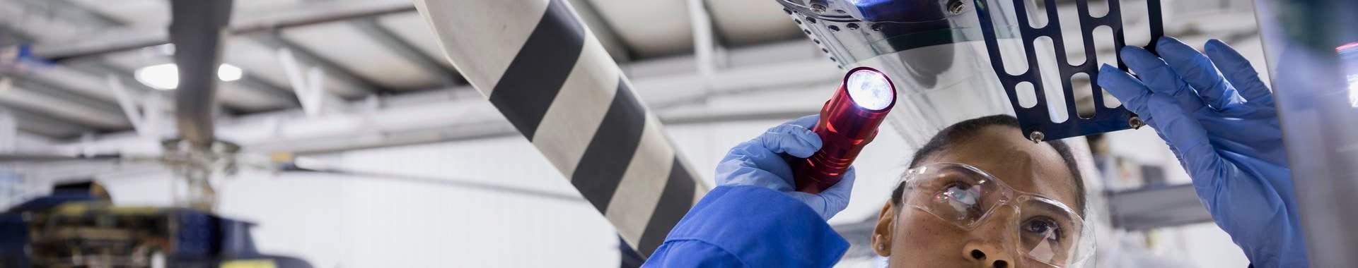 Female helicopter mechanic examining part with flashlight