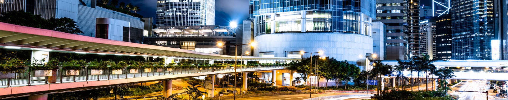 A multi-lane highway is brightly illuminated by roadway lighting, with a modern cityscape on the horizon.