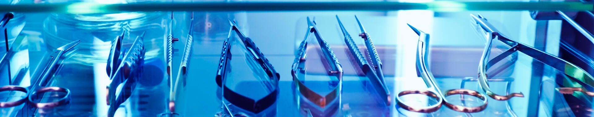 Medical tools sit on a shelf under the blue glow of ultraviolet light, used as a germicidal disinfectant.