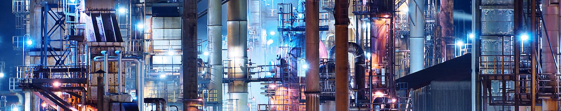 A brightly lit commercial oil refinery is shown at night.