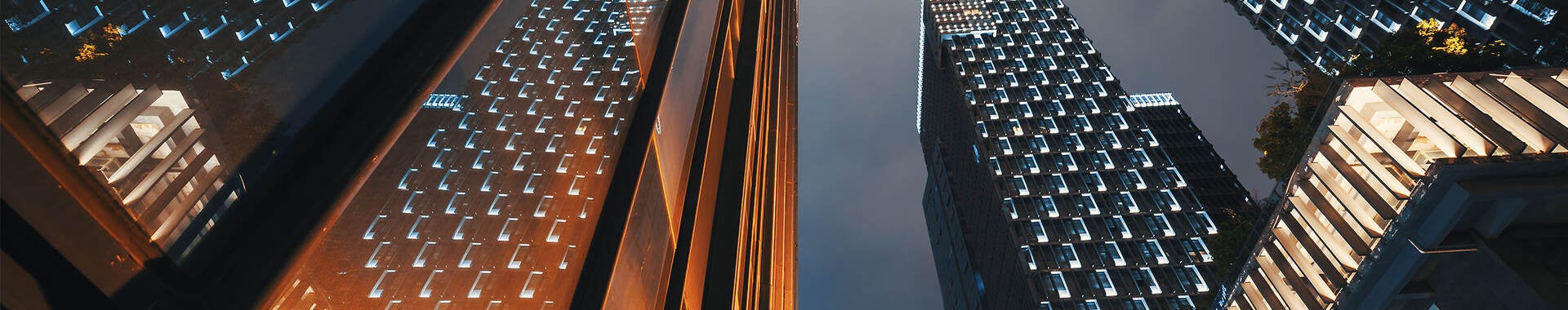 Low angle view of modern skyscraper buildings illuminated at night reflecting on a glass facade 