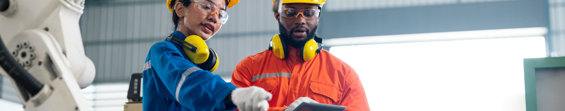 Engineers talking in a factory, with robotic arm in foreground