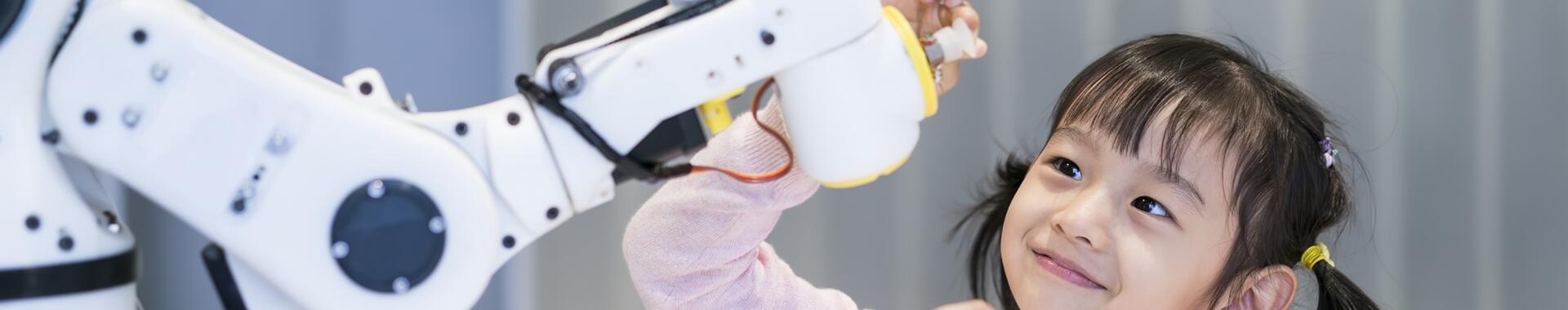 A young girl looking at a robotic arm.