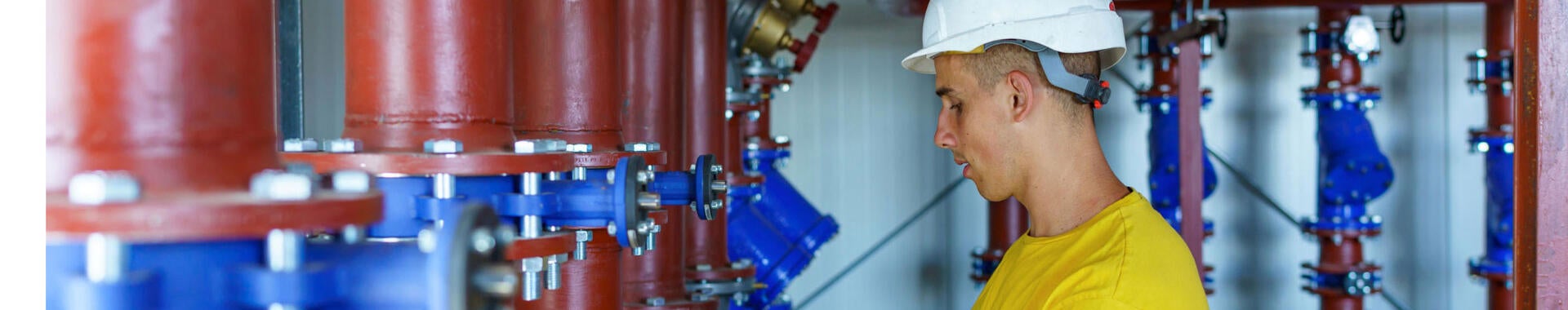 A male heating plant worker wearing a hardhat is standing next to a pipe system and performing a quality check.