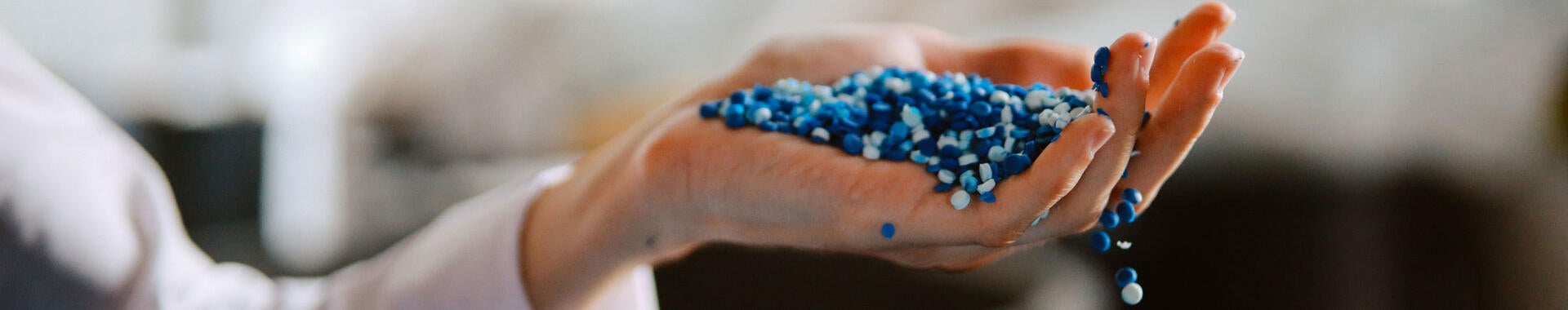 A person's hand holding blue plastic pellets