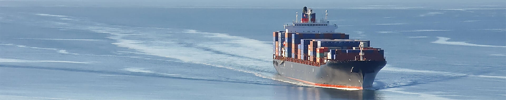 Distant aerial photo of a loaded container ship at sea.