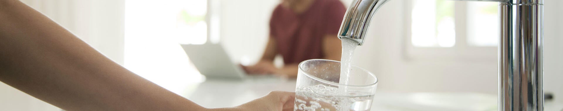 A person filling a water glass at a kitchen sink