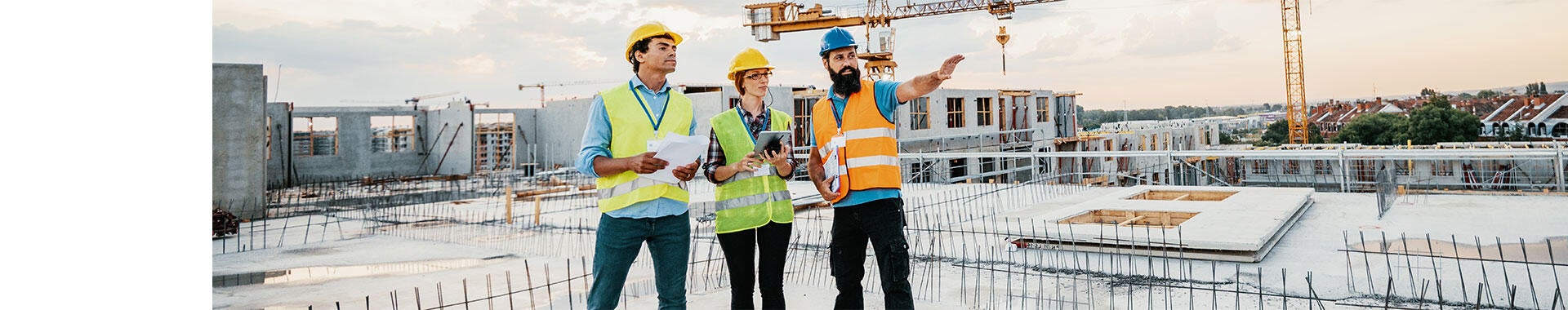 Three construction workers in safety vests and helmets reviewing plans on a building site