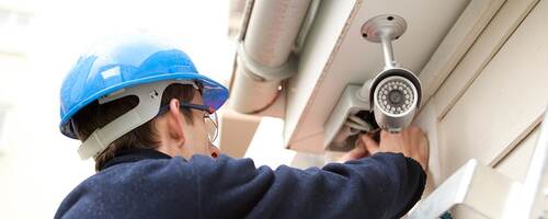 Man in hard hat on a ladder installing an outdoor security camera