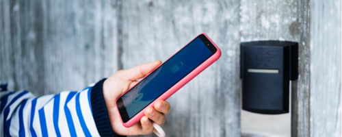 Woman in blue striped shirt holding a smart phone next to a digital lock