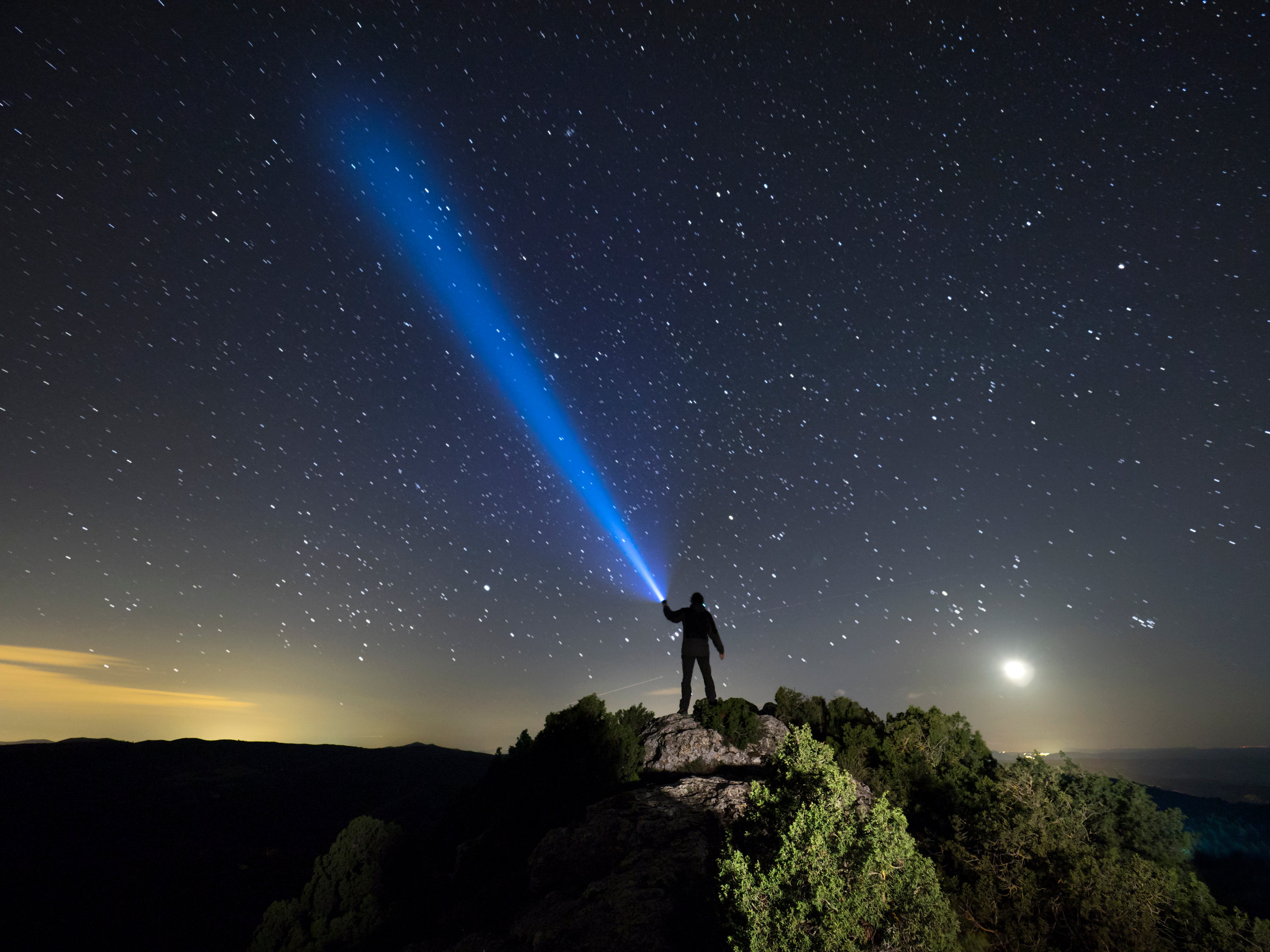 Silhouette of a man on the top of a mountain in the night, with a lantern in the hand doing a beam of light on a sky of stars