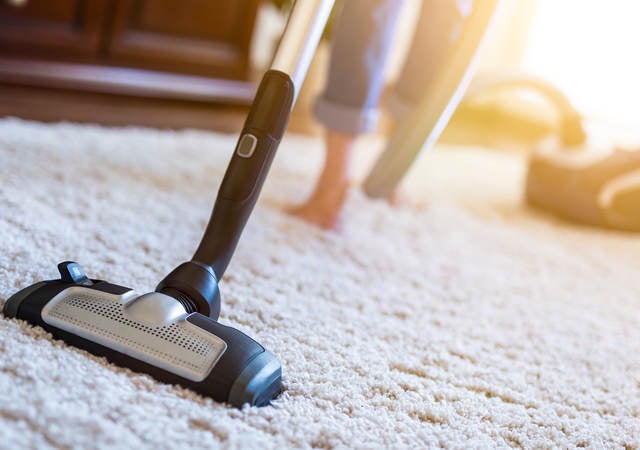 Woman using vacuum cleaner while cleaning carpet in house