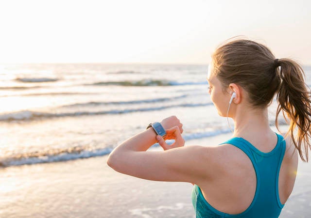 jogging woman looking at her fitness tracker with the ocean in the background