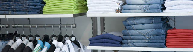 Retail store shelves filled with neatly folded clothes arranged by color. 