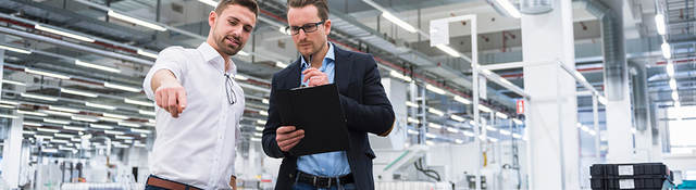 Two men consulting over pallets of plastic products