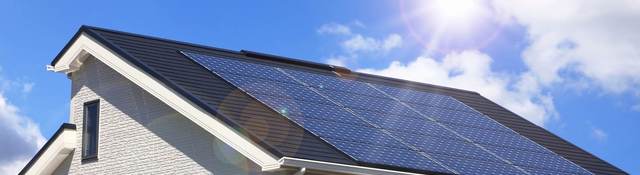 The sun shines brightly on the solar panels installed on the roof of a white, stucco home.