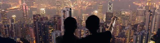 Silhouette of couple sit on ground point faraway on the roof above the city in the night.