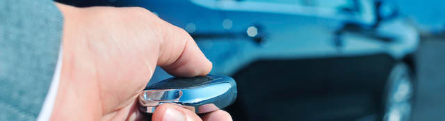 A man approaches a car with a key fob in his hand.