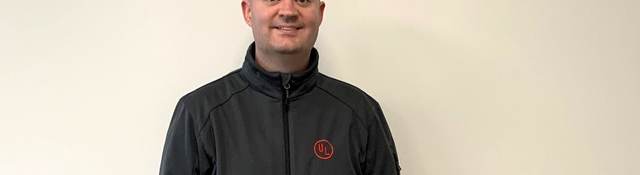 Seán Flannagan poses for EWeek picture. He's wearing a dark grey jacket with the red UL logo on its left pocket.