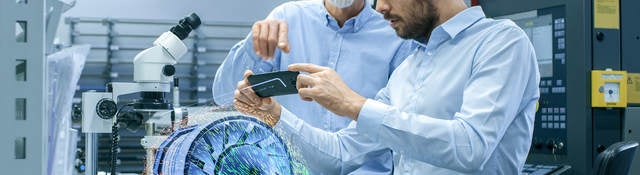 Two Engineers Works with Mobile Phone Using Augmented Reality Holographic Projection 3D Model of the Engine Turbine Prototype